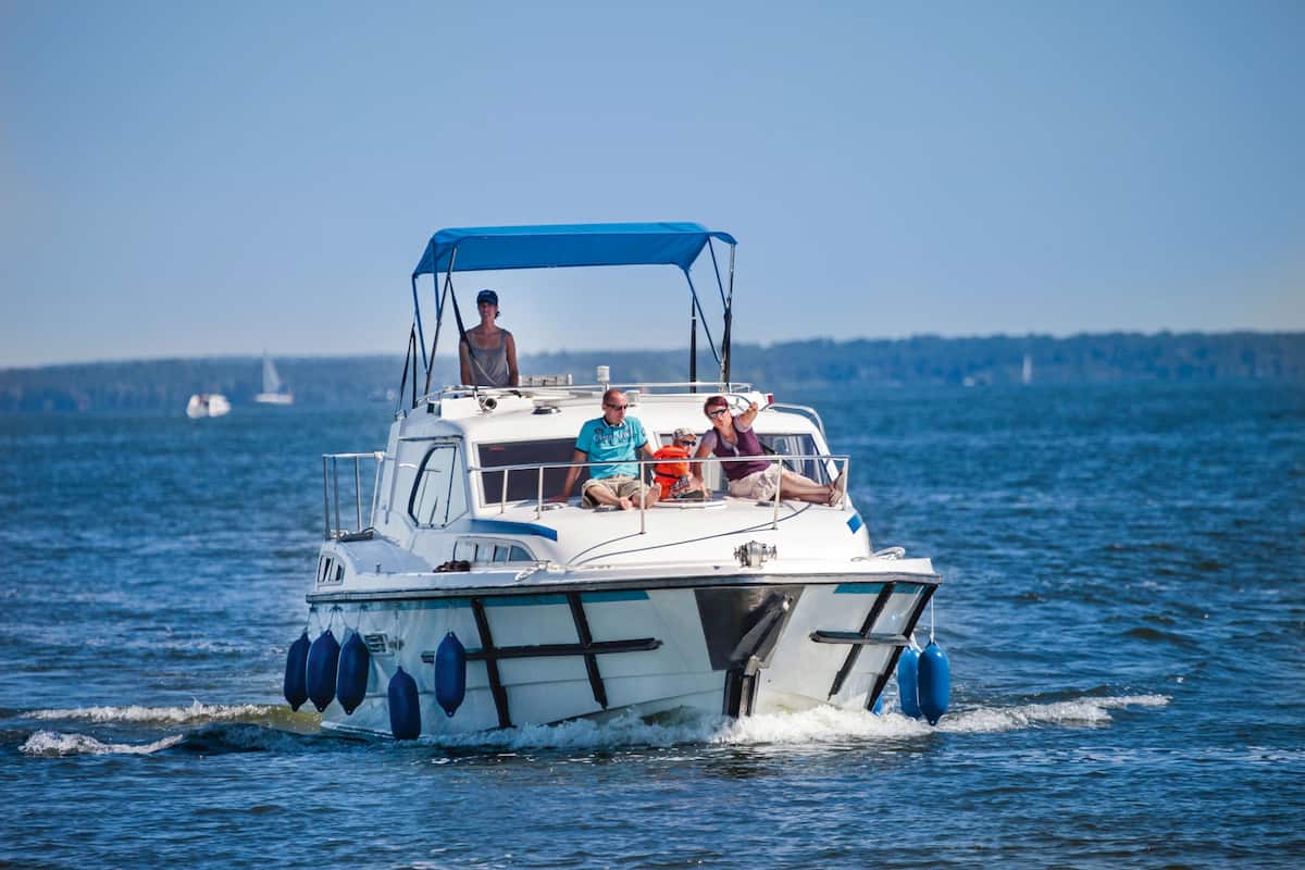 A boat with a blue canopy, passengers, and a clear view of the water and distant shoreline.