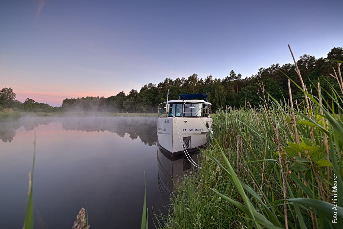 A boat docked at a calm river with dense greenery on the banks.