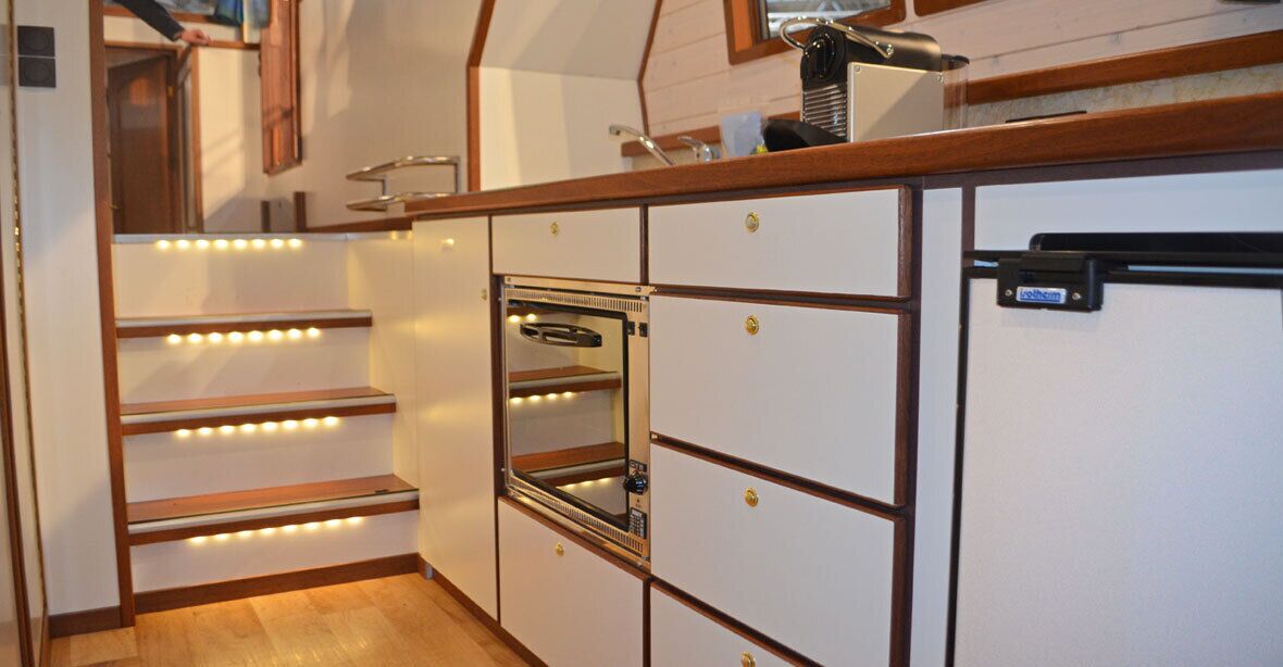 A compact kitchen with built-in appliances, wooden shelves, and a small refrigerator.