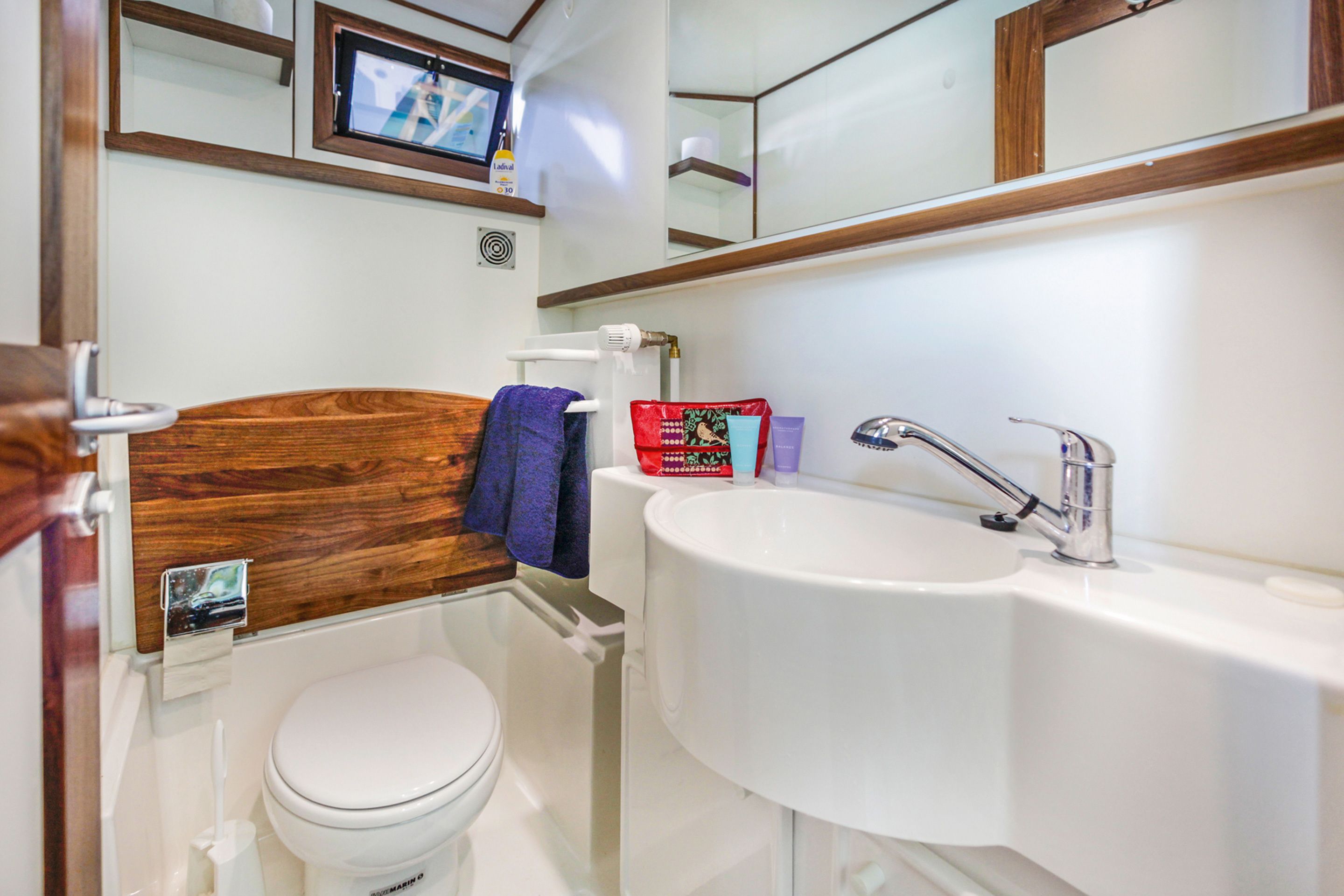 A bathroom with a wooden headboard, a white toilet, a sink with a faucet, and a mirror above the sink.