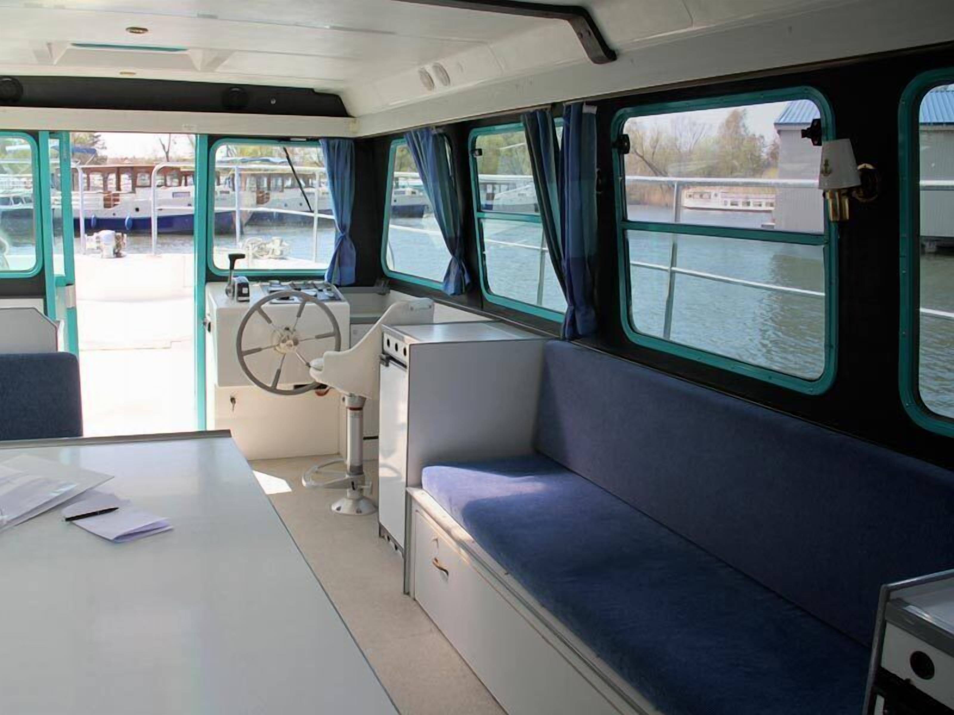 A boat interior with a control station, seating area, and windows overlooking the water.