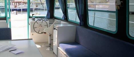 A boat interior with a control station, seating area, and windows overlooking the water.