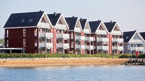 Una hilera de edificios de varios pisos, con balcones, en rojo y blanco, frente a una playa arenosa y el agua.