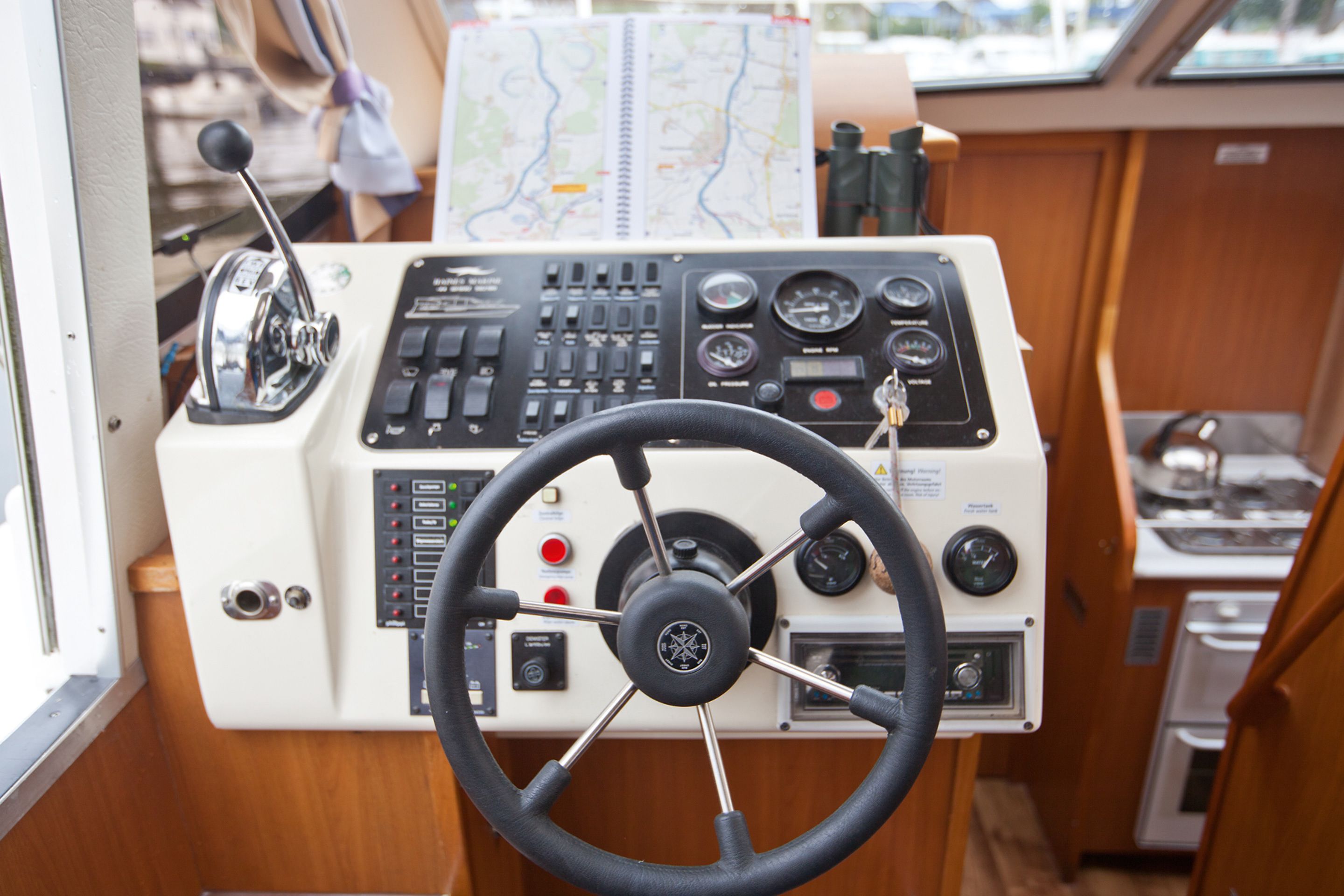 Bedieningspaneel van een boot met een stuurwiel, diverse meetinstrumenten en een kaart.