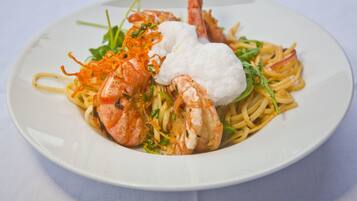 Une assiette de pâtes aux crevettes, garnie d’une cuillère de crème et accompagnée de quelques légumes verts.