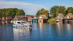 Una casa flotante amarrada cerca de una hilera de casas tradicionales a orillas de un río tranquilo.