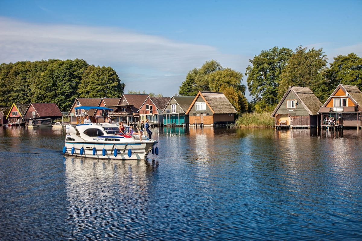A houseboat docked near a row of traditional houses by a calm river.
