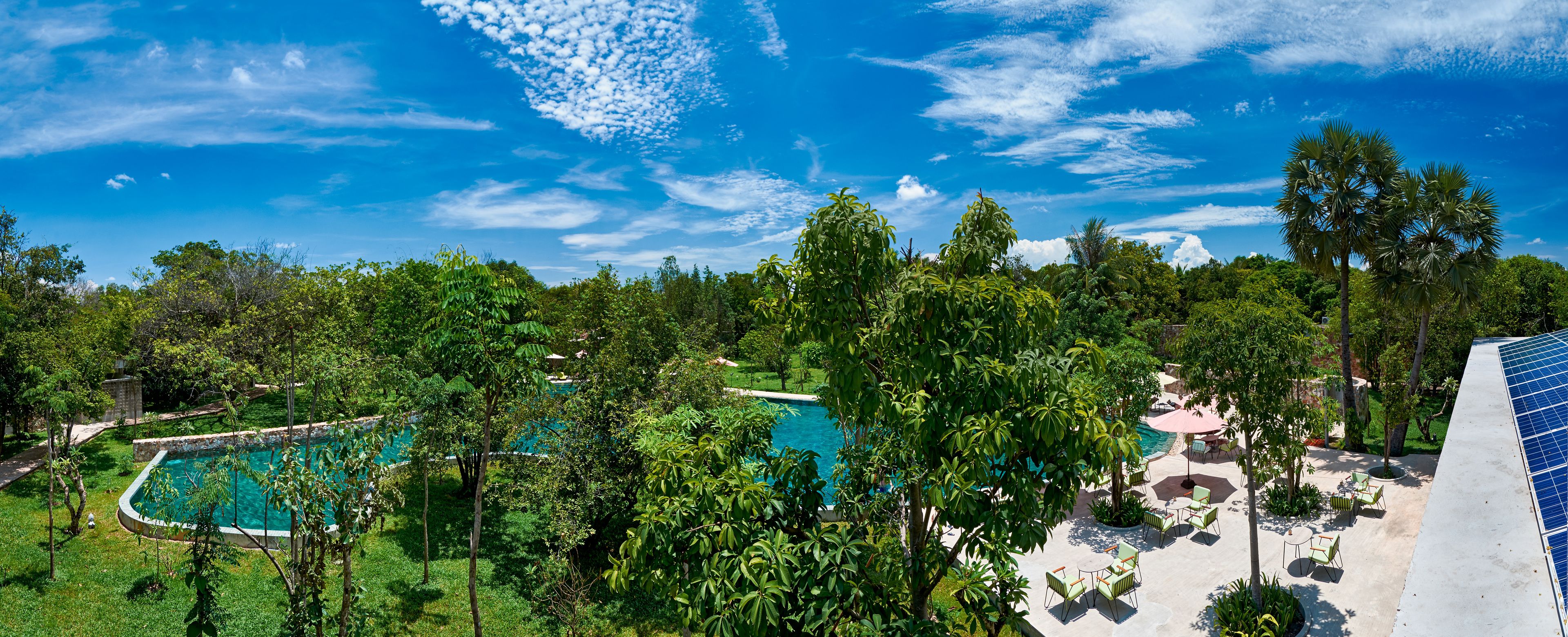 A pool surrounded by lush greenery, outdoor seating, and a clear blue sky.