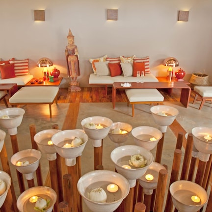 A serene room with a sofa set, a Buddha statue, and multiple bowls with candles.