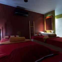 Two single beds with red bedding and a beige throw blanket, a wooden ladder, and a wall-mounted air conditioning unit.
