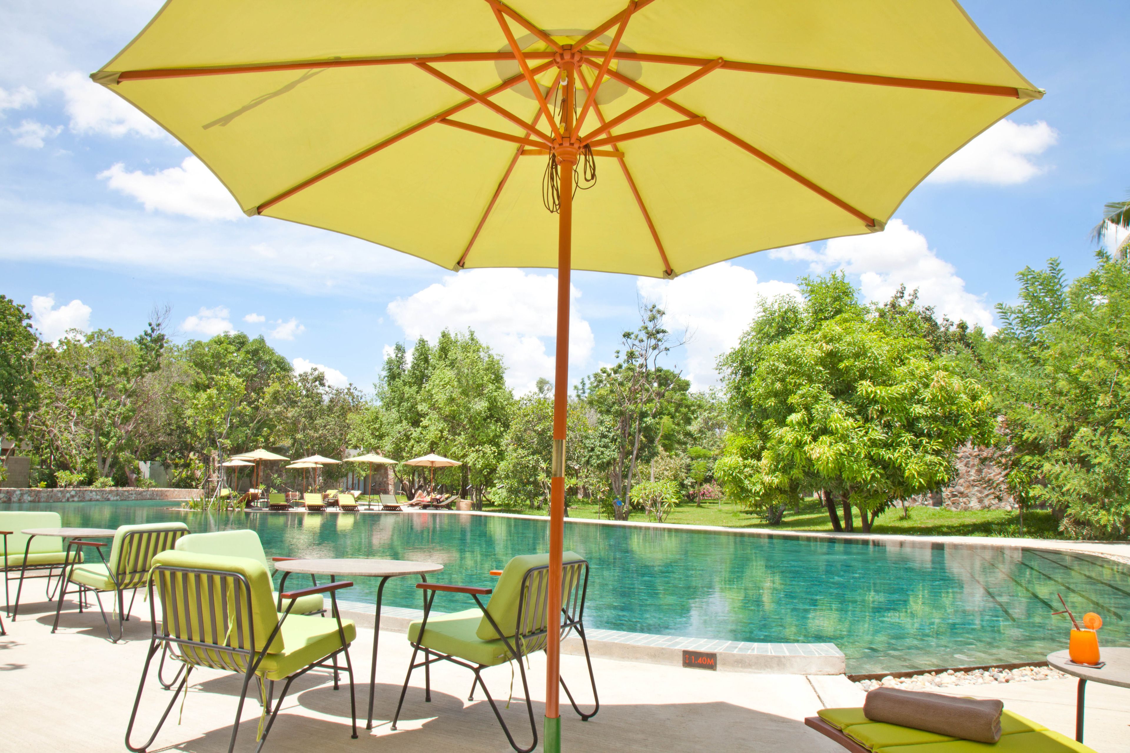 A pool area with lounge chairs and a large umbrella.