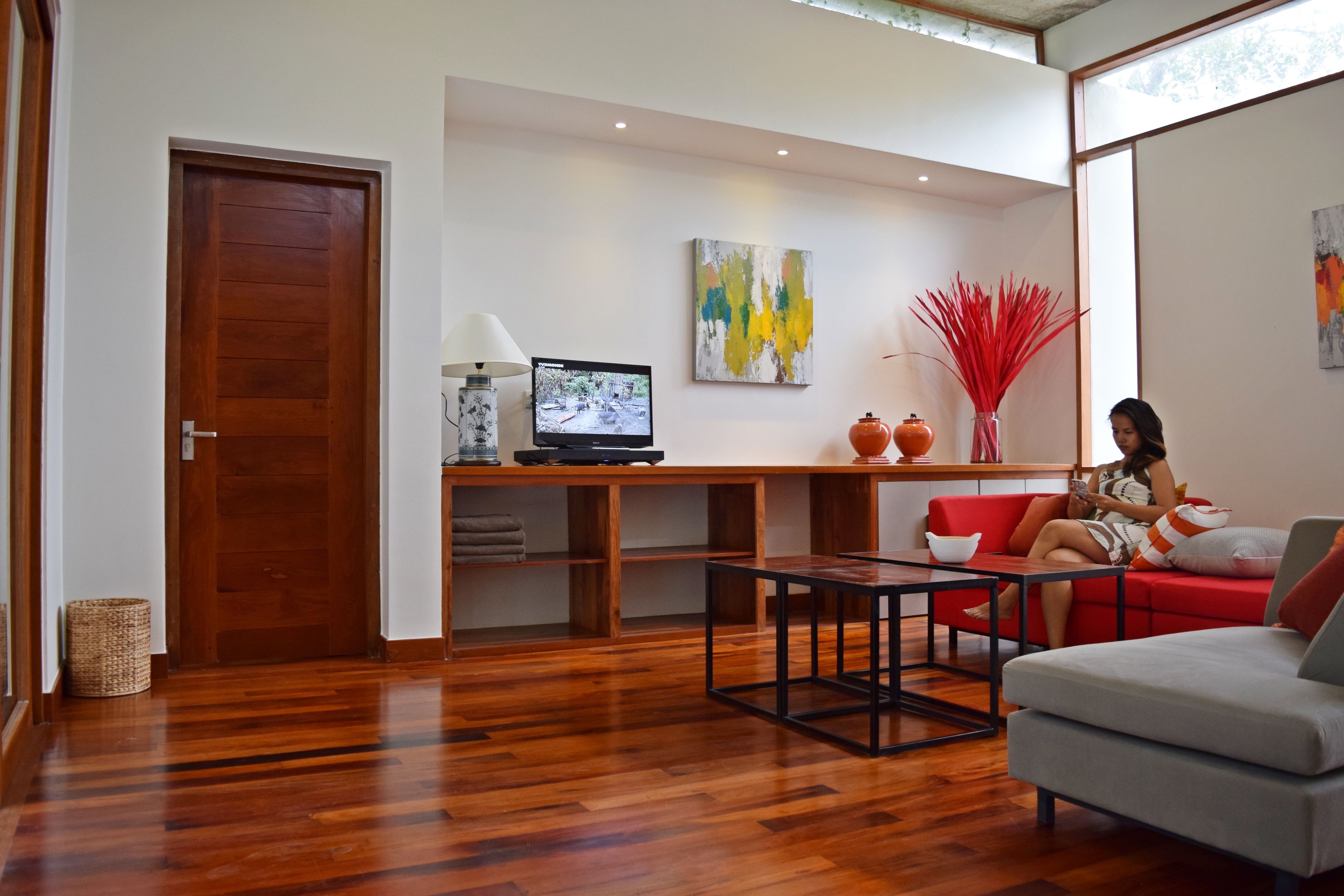 Een moderne woonkamer met een houten vloer, een rode bank, een grijze bank, een salontafel, een televisie en kunstwerken aan de wanden.