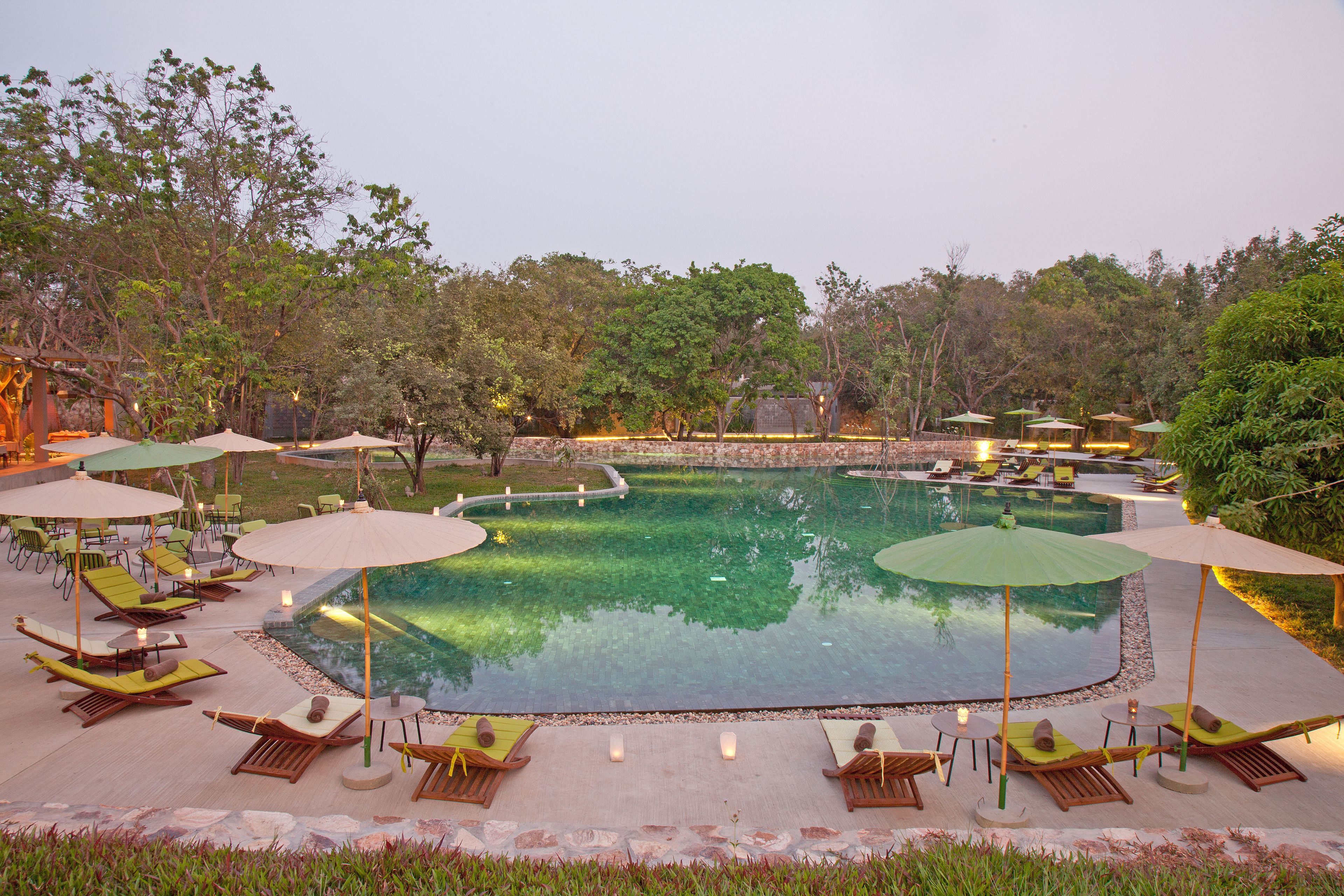 A pool area with lounge chairs and umbrellas, surrounded by trees and a stone wall.