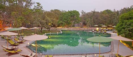 A pool area with lounge chairs and umbrellas, surrounded by trees and a stone wall.