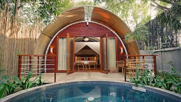 A poolside area with a covered seating area, bamboo fence, and a pool.