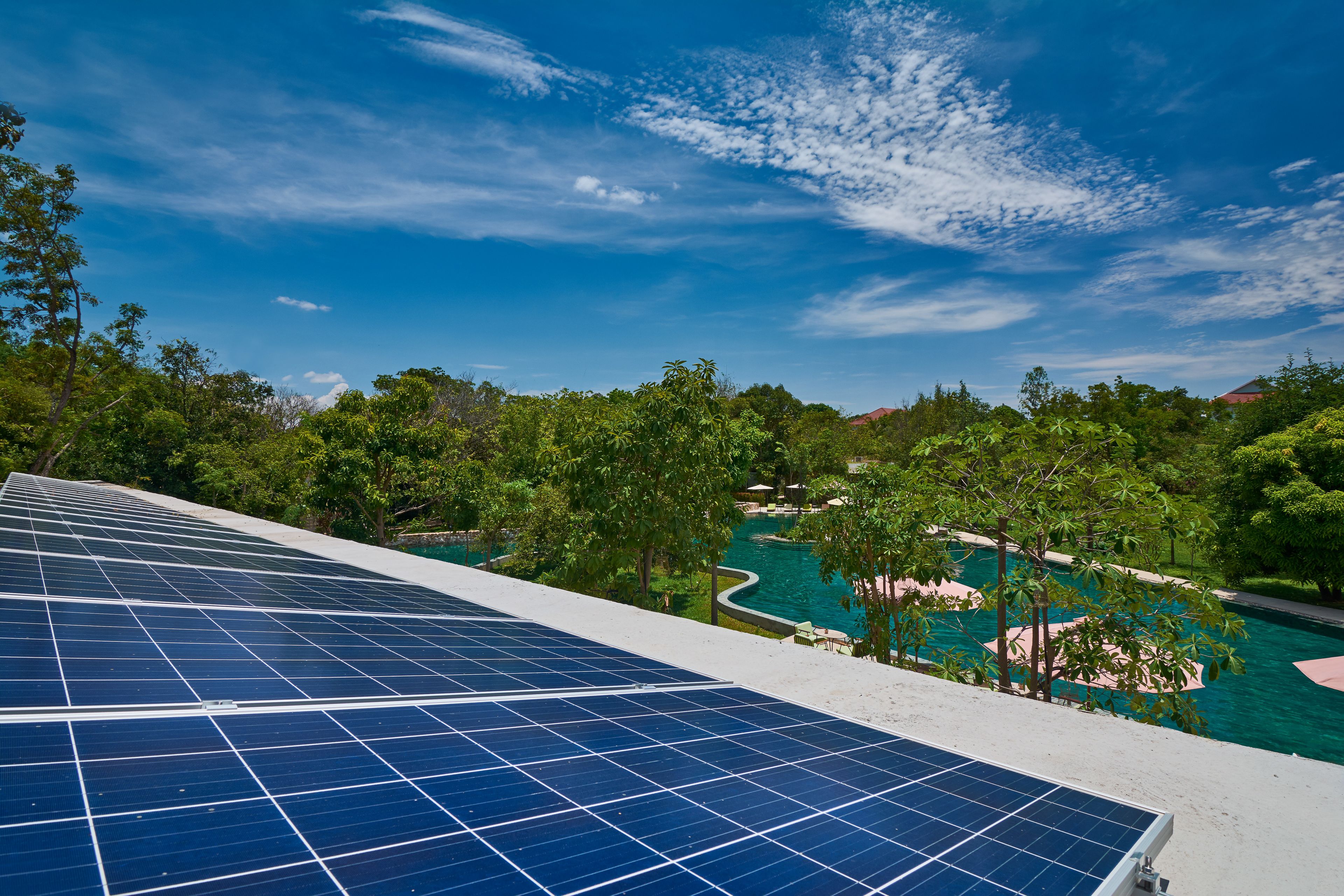 Des panneaux solaires sur un toit surplombent une zone avec piscine, des arbres et un ciel dégagé.