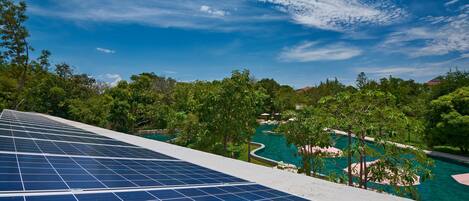 Des panneaux solaires sur un toit surplombent une zone avec piscine, des arbres et un ciel dégagé.
