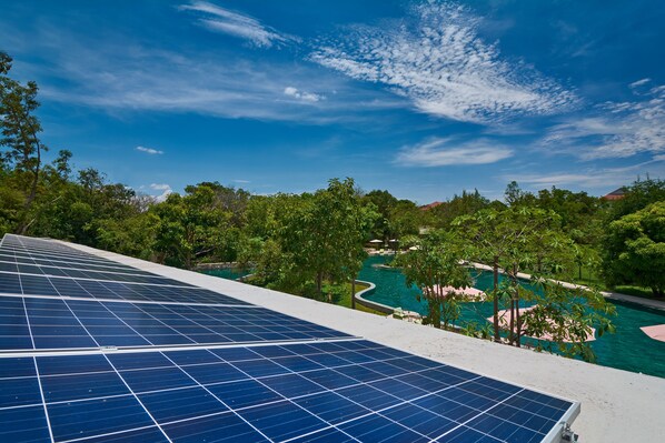 Solar panels on a rooftop overlooking a pool area with trees and a clear sky. - Templation Hotel (Siem Reap)