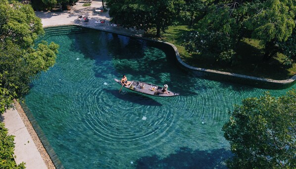 A clear pool with a boat, surrounded by trees and a paved walkway.