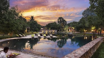 Relax by the tranquil pool surrounded by lush greenery and lounge chairs.