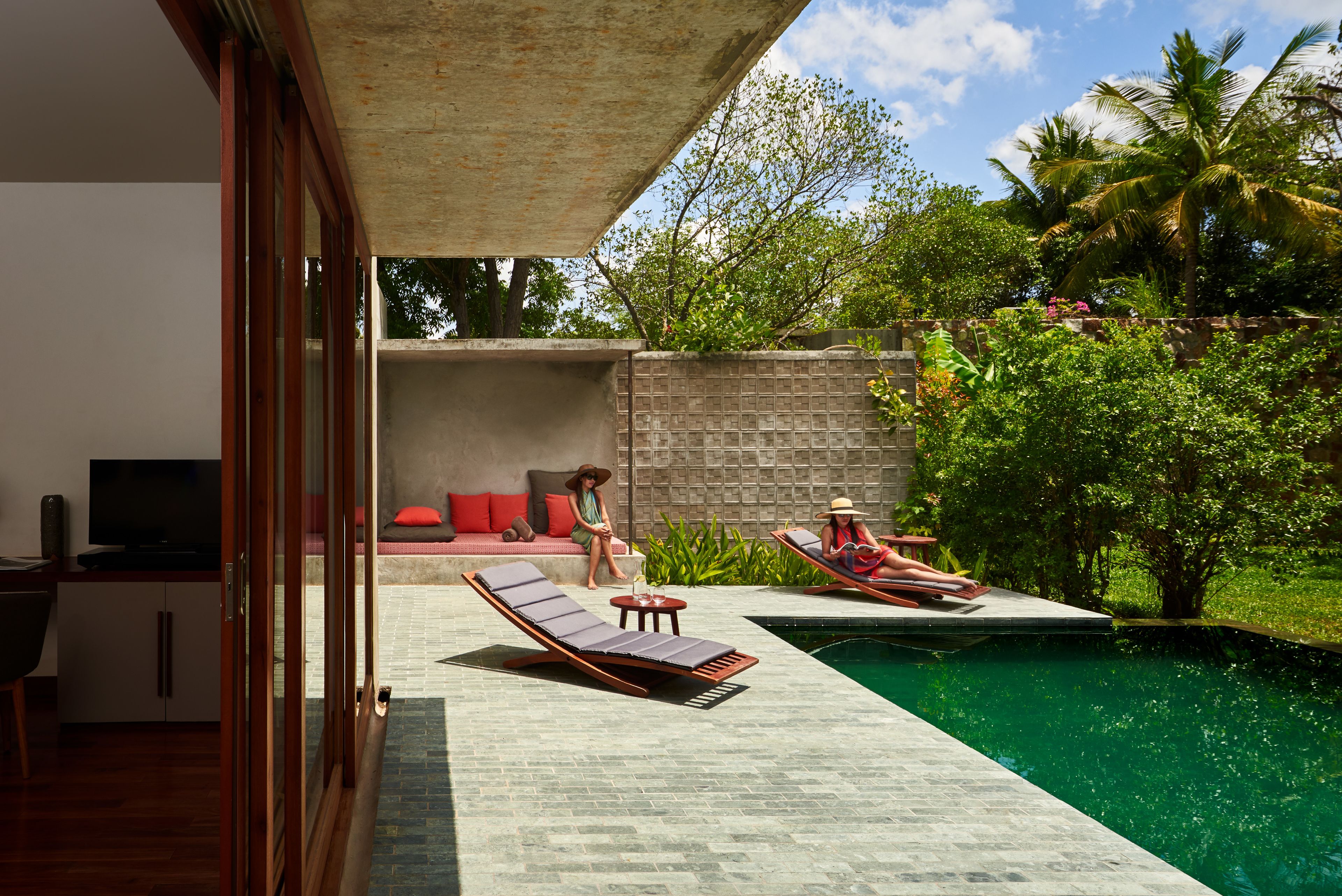 A modern outdoor pool area with lounge chairs and a seating area with a TV.