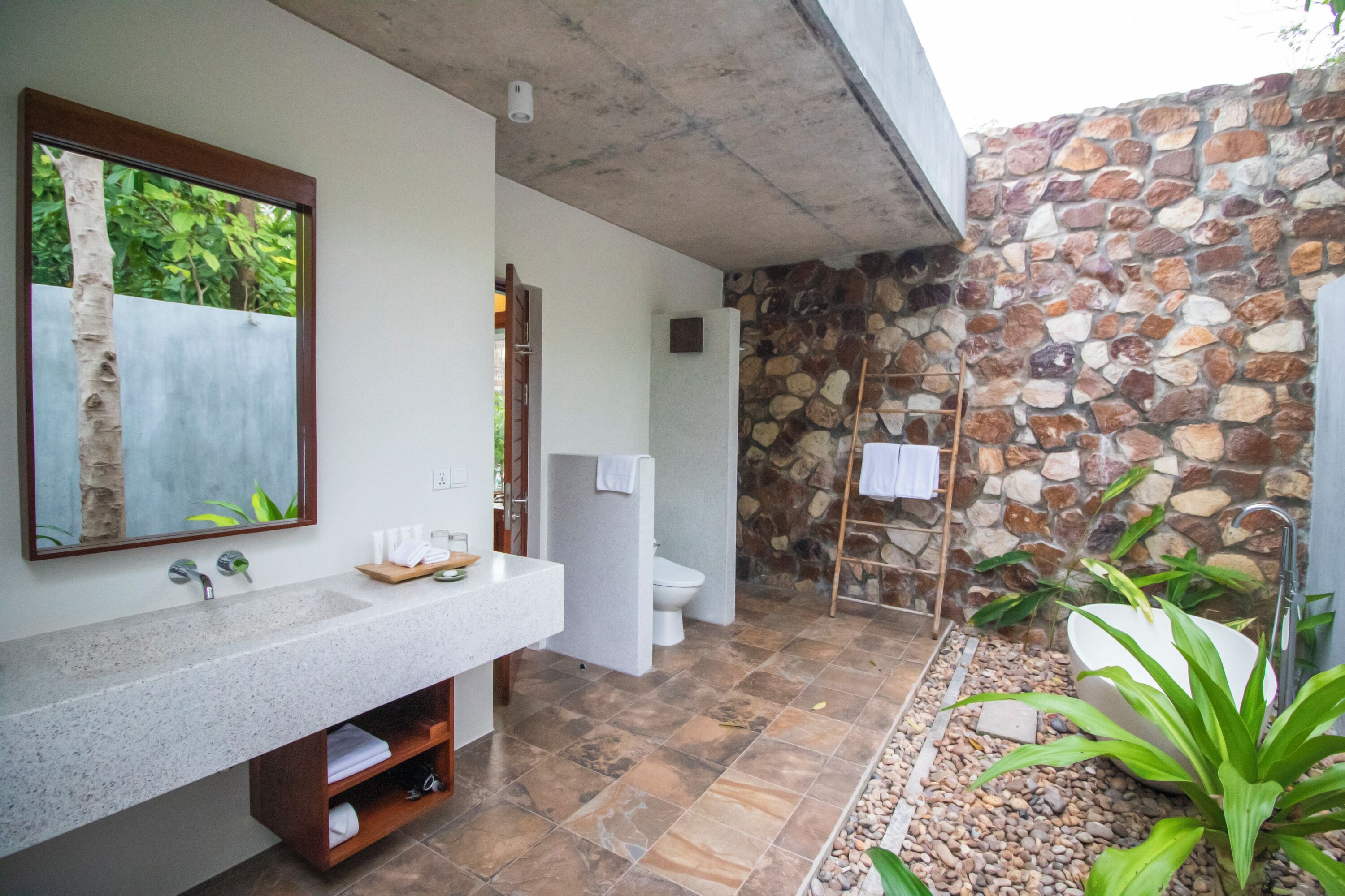 Un baño moderno con pared de piedra, un lavamanos grande y una bañera.