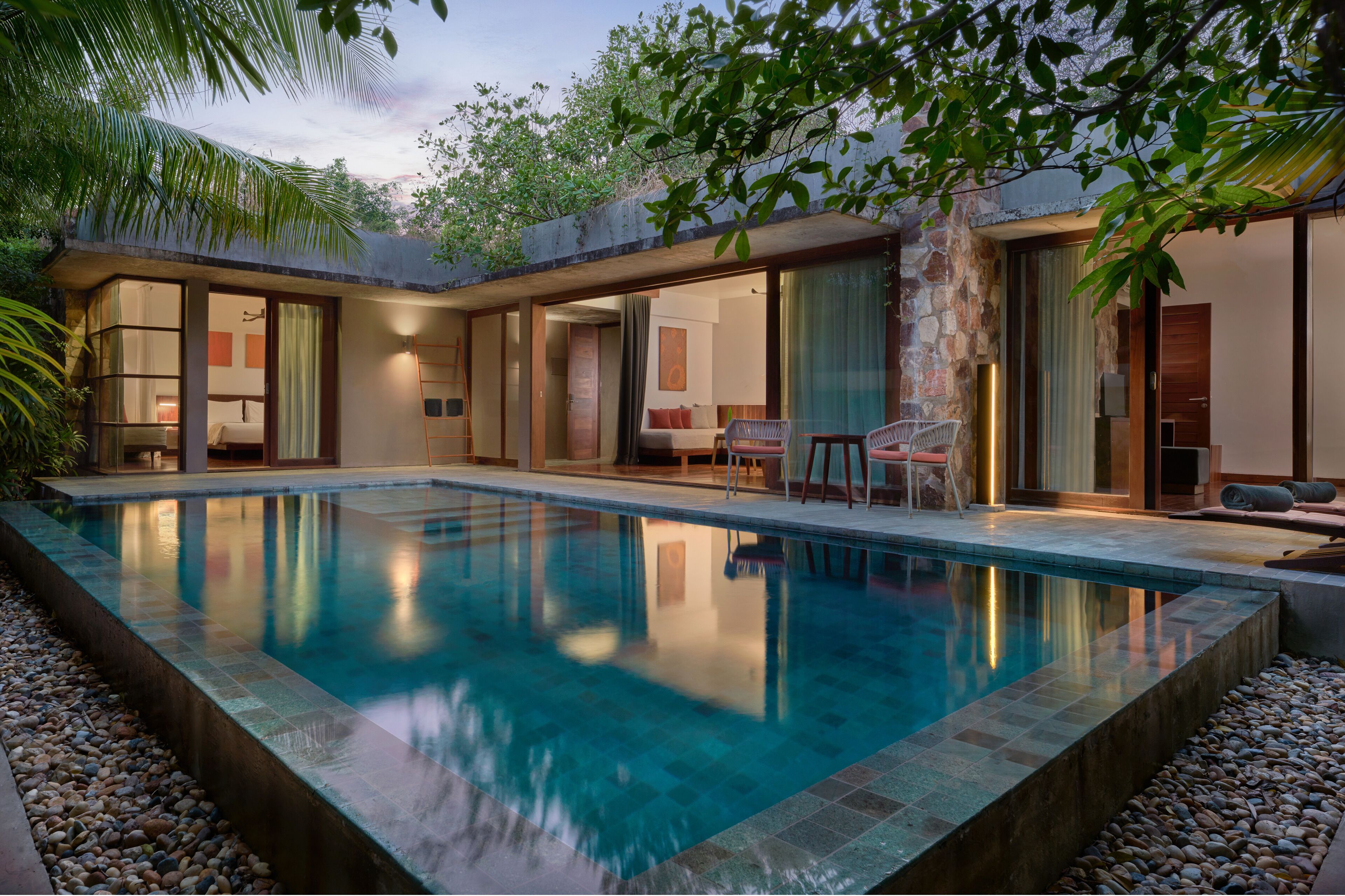 A modern pool area with a clear pool, stone walls, and a covered seating area with chairs and a table.