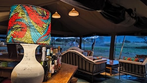 A tented outdoor seating area with a table, chairs, and a decorative lamp. - Kananga Special Tented Camp (Serengeti)