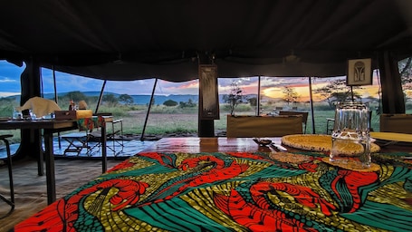 An interior view of a tent with a table set for dining, a large window offering a view of the landscape, and a speaker in the center.