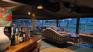 An indoor tent with a bar area, seating, and a view of the outdoors. - Kananga Special Tented Camp (Serengeti)