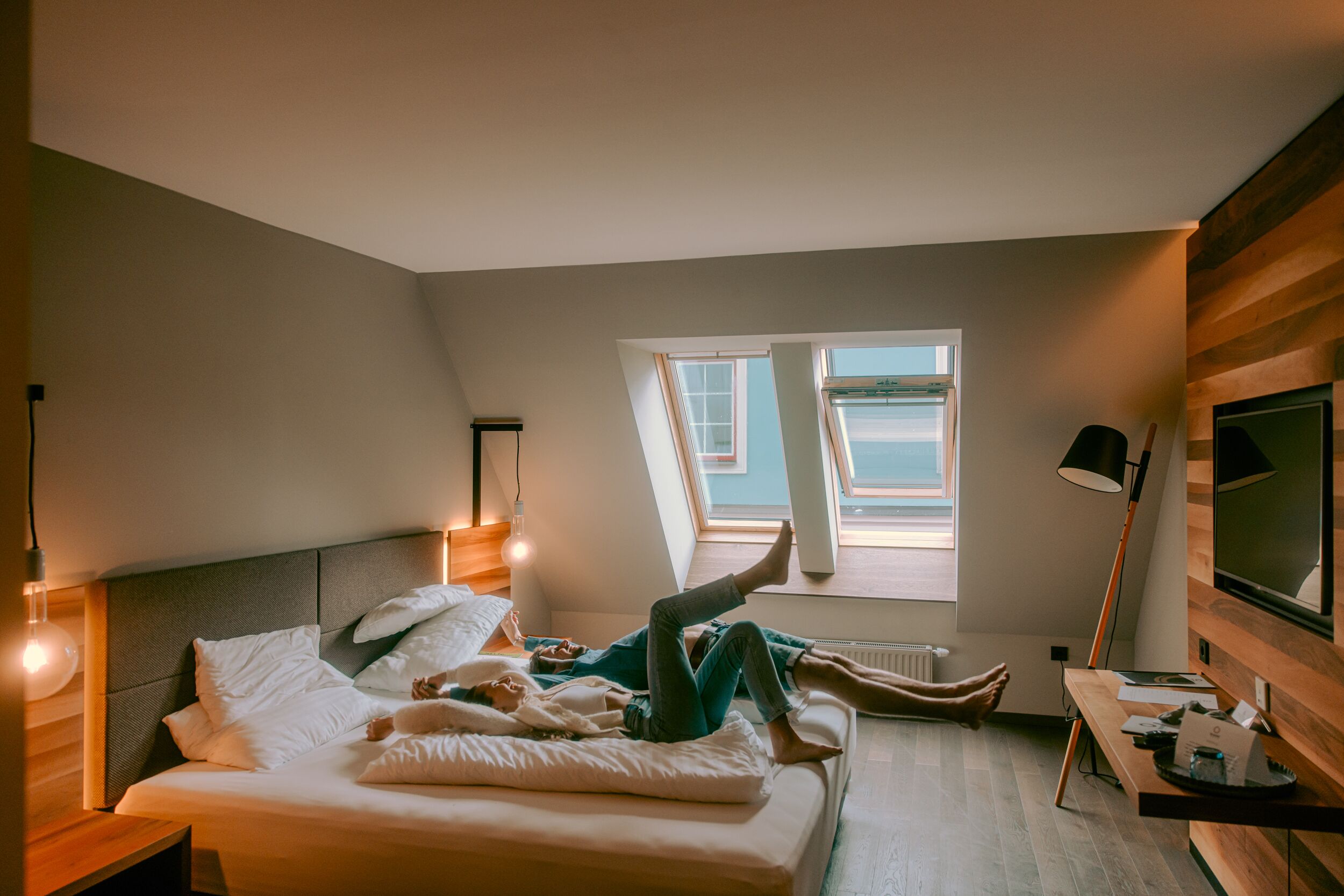 A bedroom with a bed, a desk, a TV, and a window with a view.