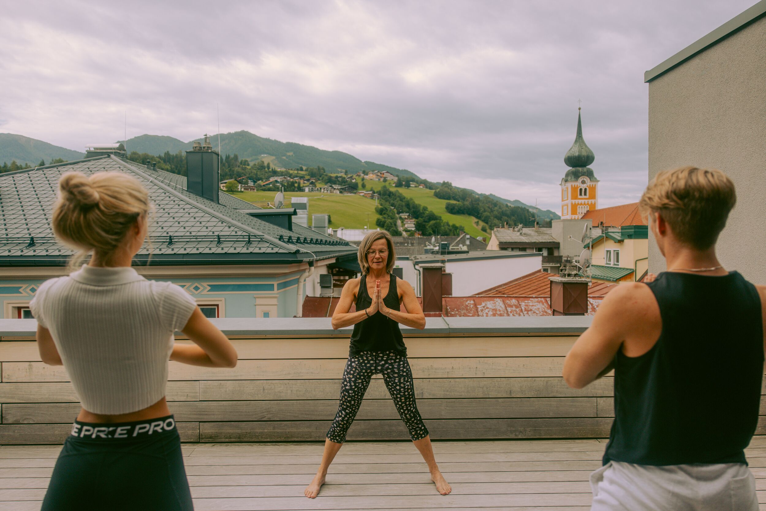 A person performing a yoga pose on a rooftop with a view of a town and mountains in the background.