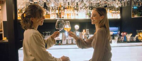Dos personas brindando con copas de vino en un bar con una amplia variedad de botellas y copas a la vista.
