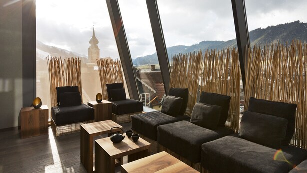 A modern lounge with a view of a distant tower and mountains. - Stadthotel brunner (Schladming)