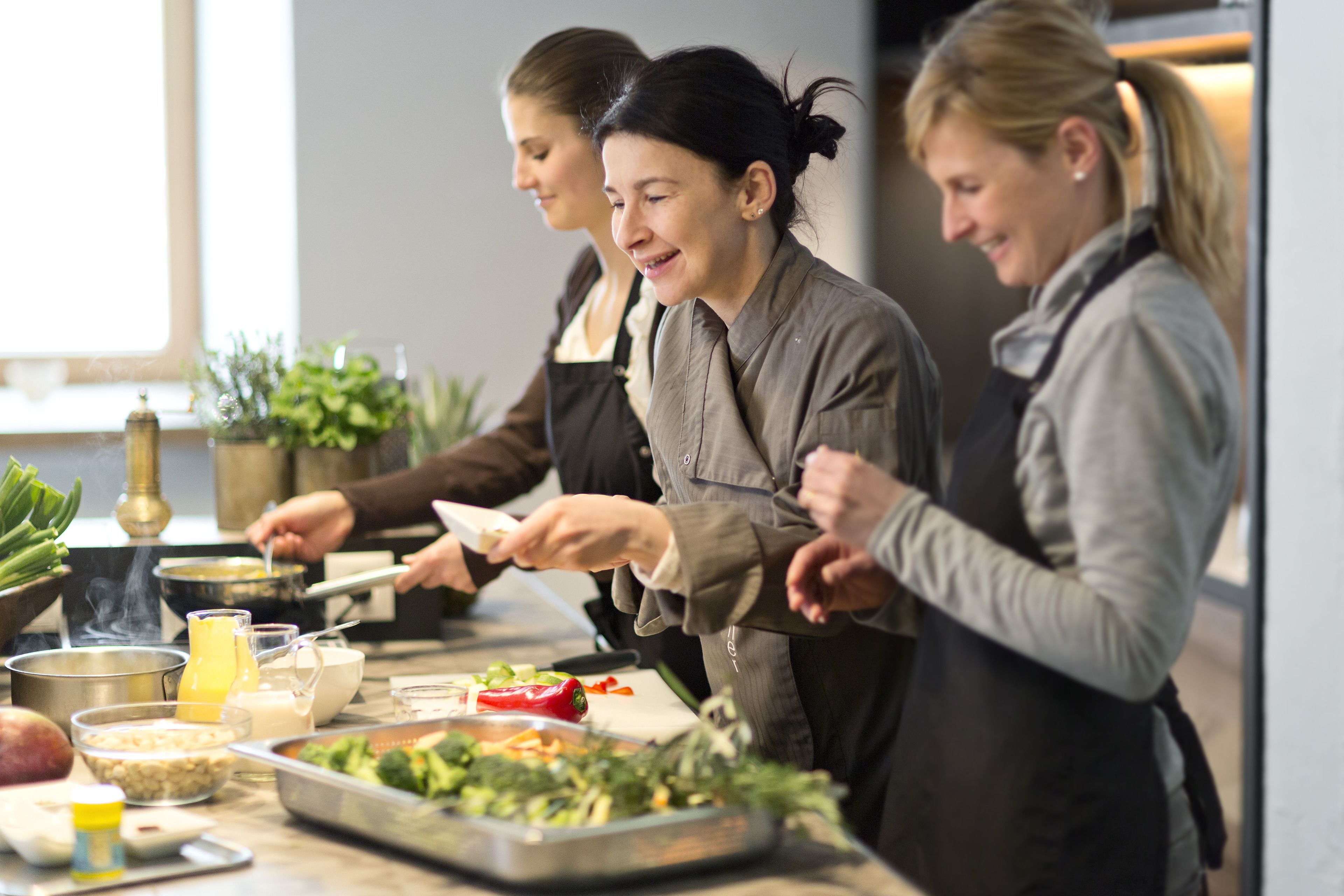 A group of people preparing food in a kitchen with various ingredients and cooking utensils on the counter.