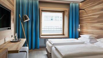 Habitación de hotel con pared de madera, un escritorio con lámpara, cama con almohadas y una ventana con cortinas.