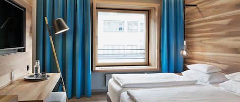 A hotel room with a wooden wall, a desk with a lamp, a bed with pillows, and a window with curtains.