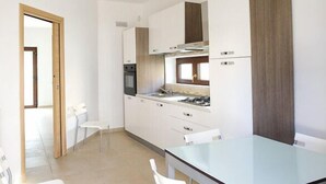 Una cocina moderna con armarios blancos, un lavamanos de acero inoxidable y una mesa de comedor de vidrio.
