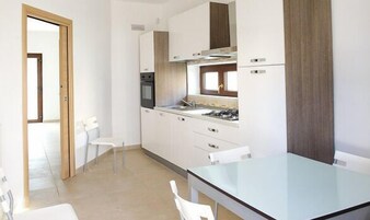 A modern kitchen with white cabinets, a stainless steel sink, and a glass dining table.