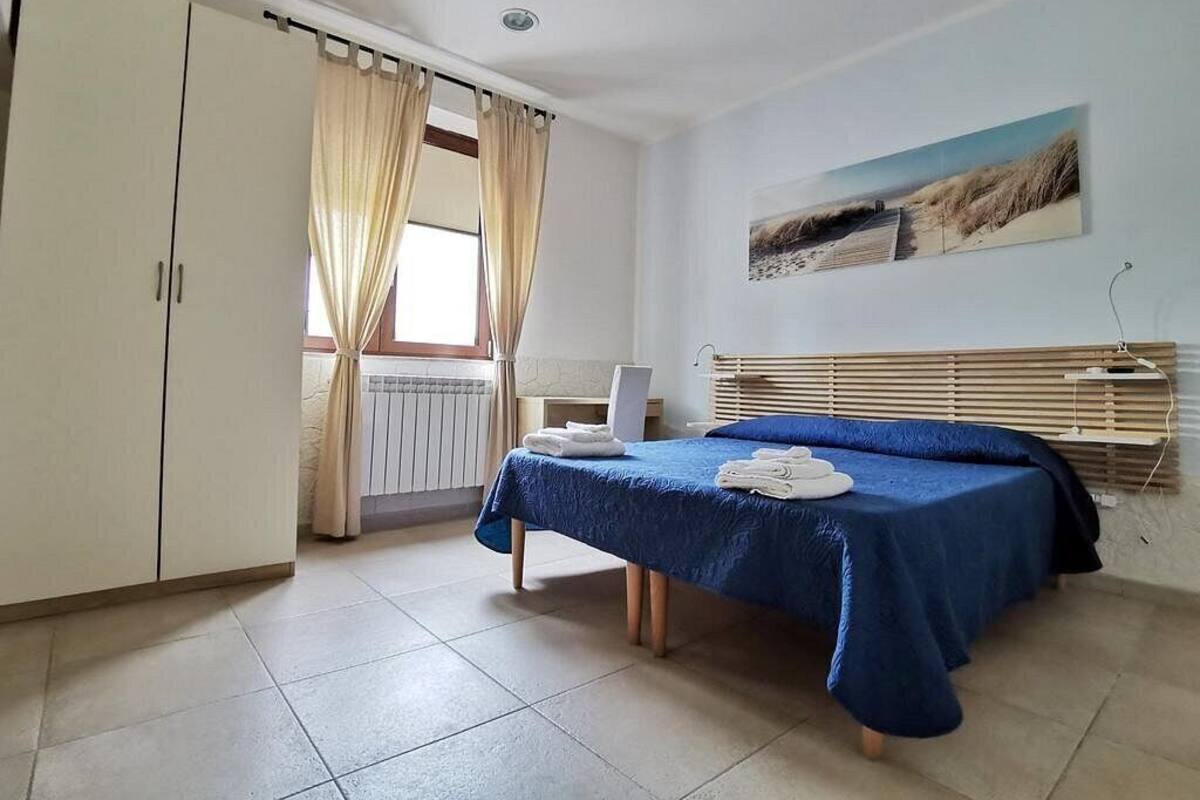 A bedroom with a bed, a desk, a chair, a wardrobe, and a window with curtains.