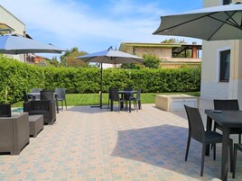 Un patio al aire libre con piso de baldosas, mobiliario exterior y sombrillas que dan sombra.
