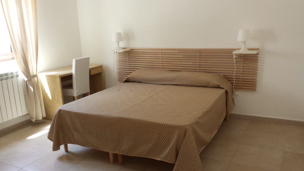A bedroom with a bed, bedside lamps, a desk, and a chair.