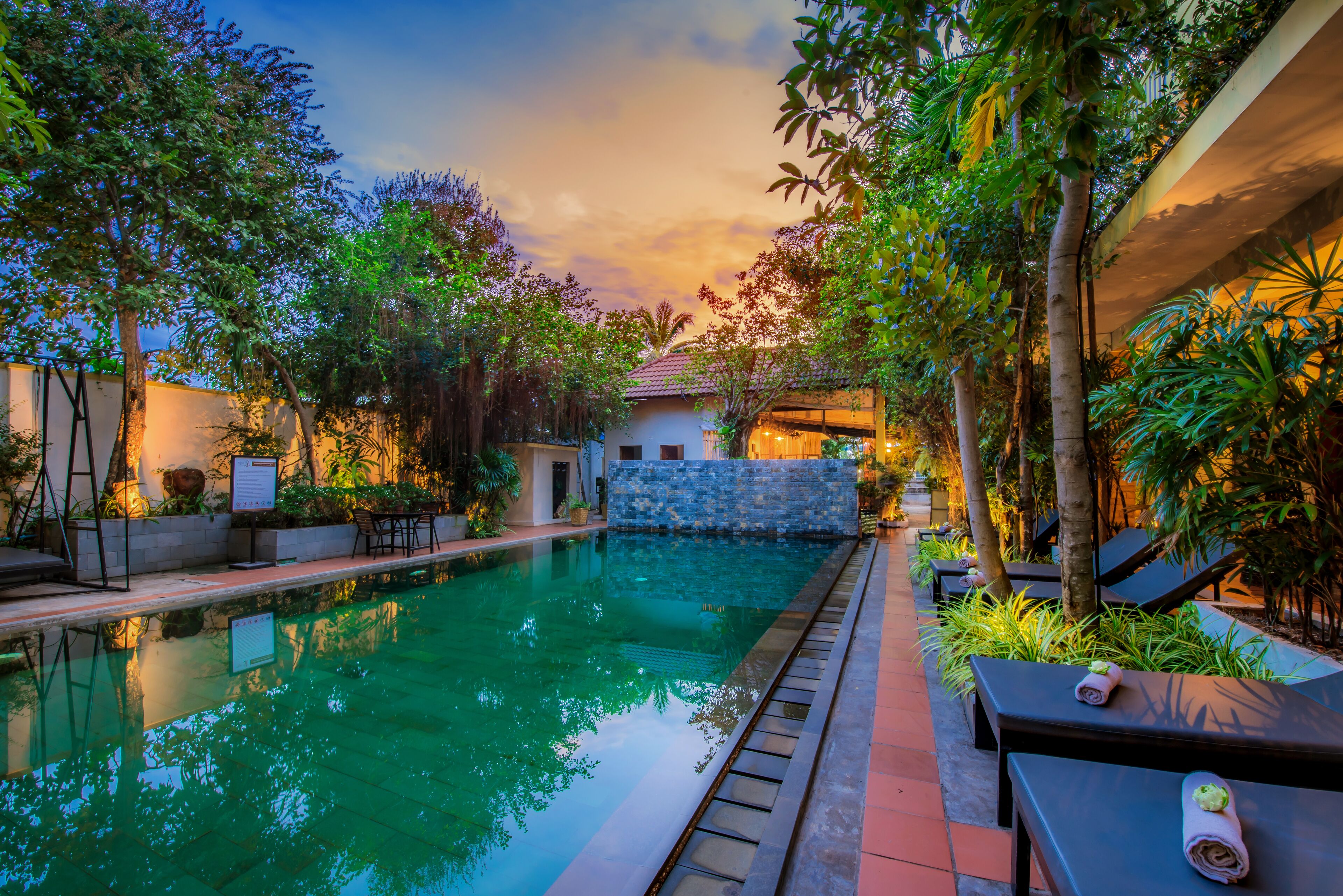 A swimming pool with lounge chairs and a stone wall, surrounded by greenery.