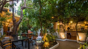 An indoor courtyard with a dining area, seating, and a large tree. - Indra Porak Residence Hotel (Siem Reap)