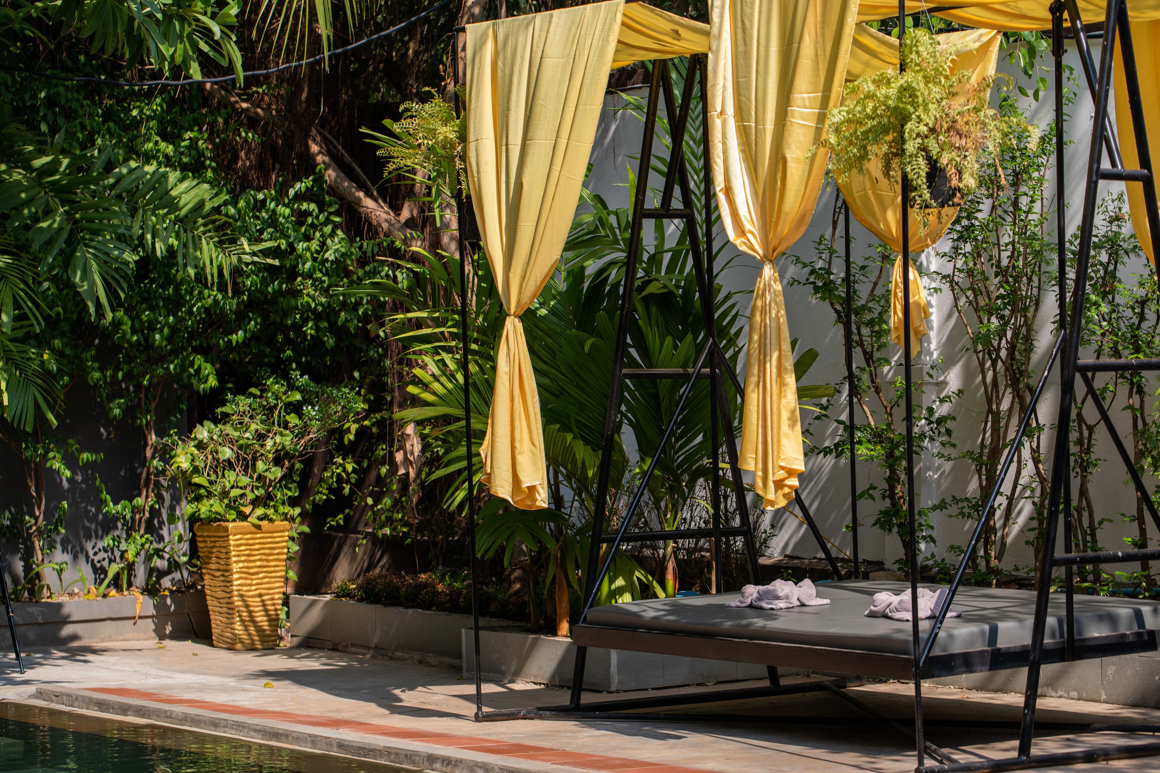 A hammock bed with yellow curtains, a small pool, and lush greenery.