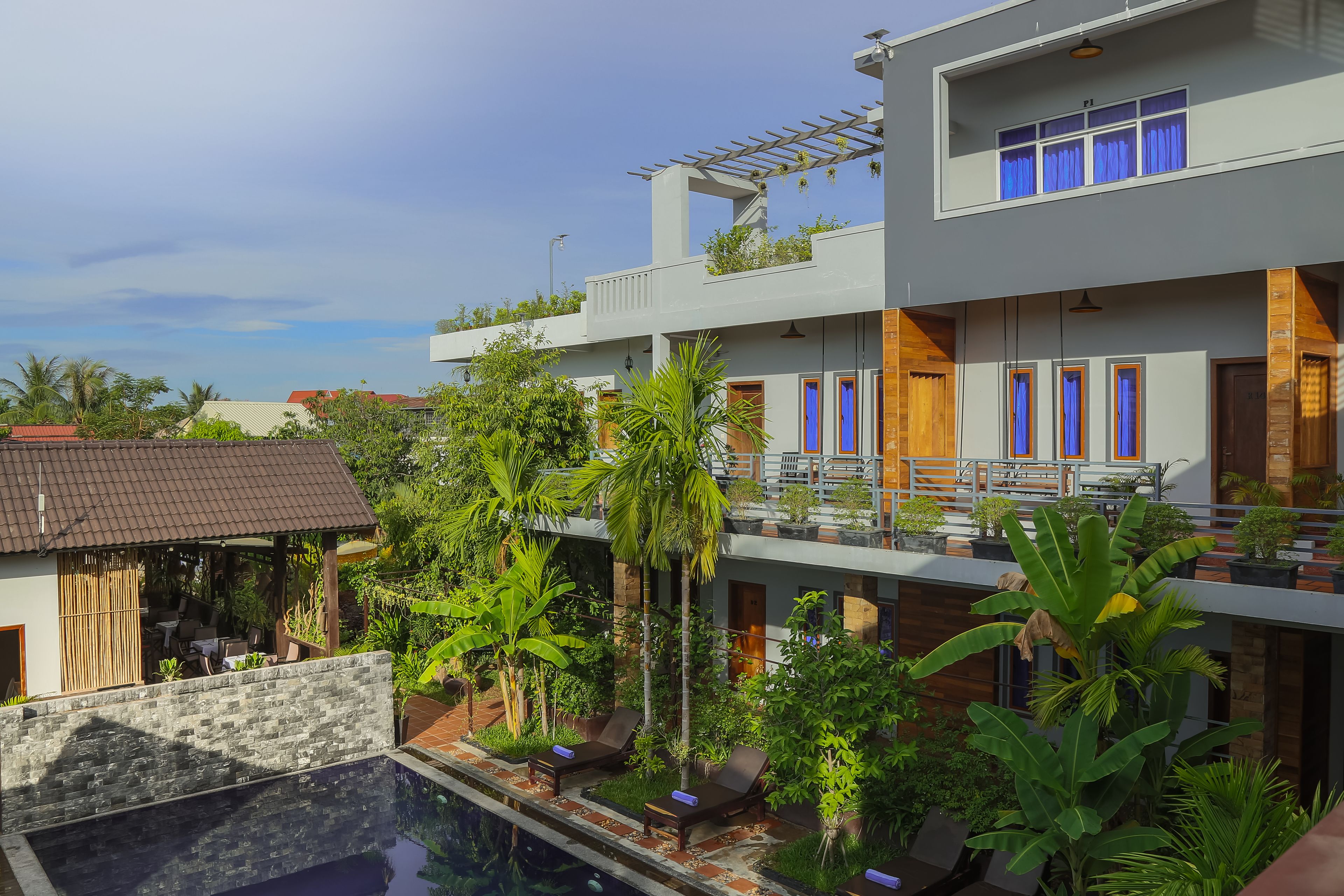 A modern hotel with a pool, outdoor seating, and lush greenery.