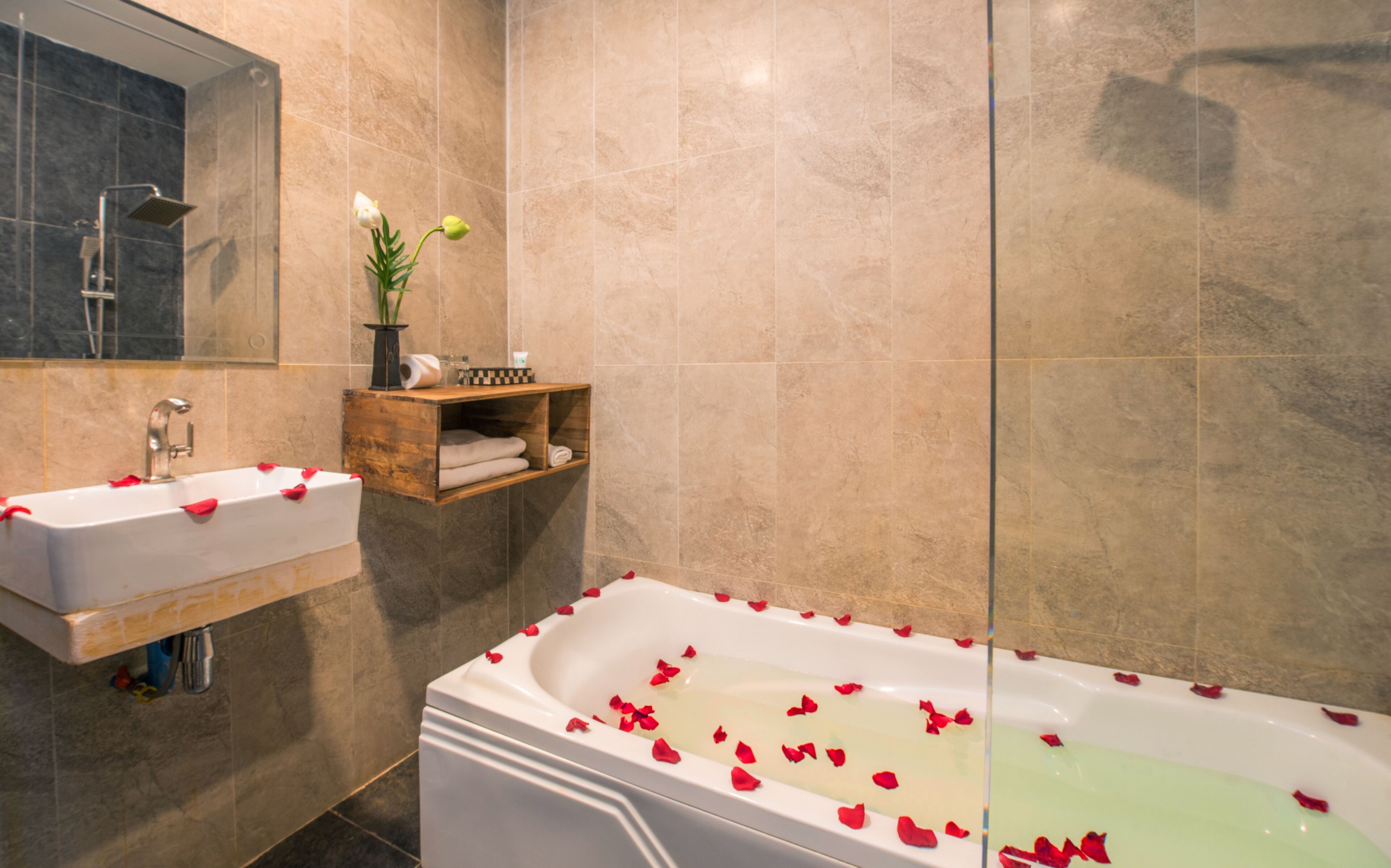 A bathroom with a bathtub filled with rose petals, a sink, and a mirror.