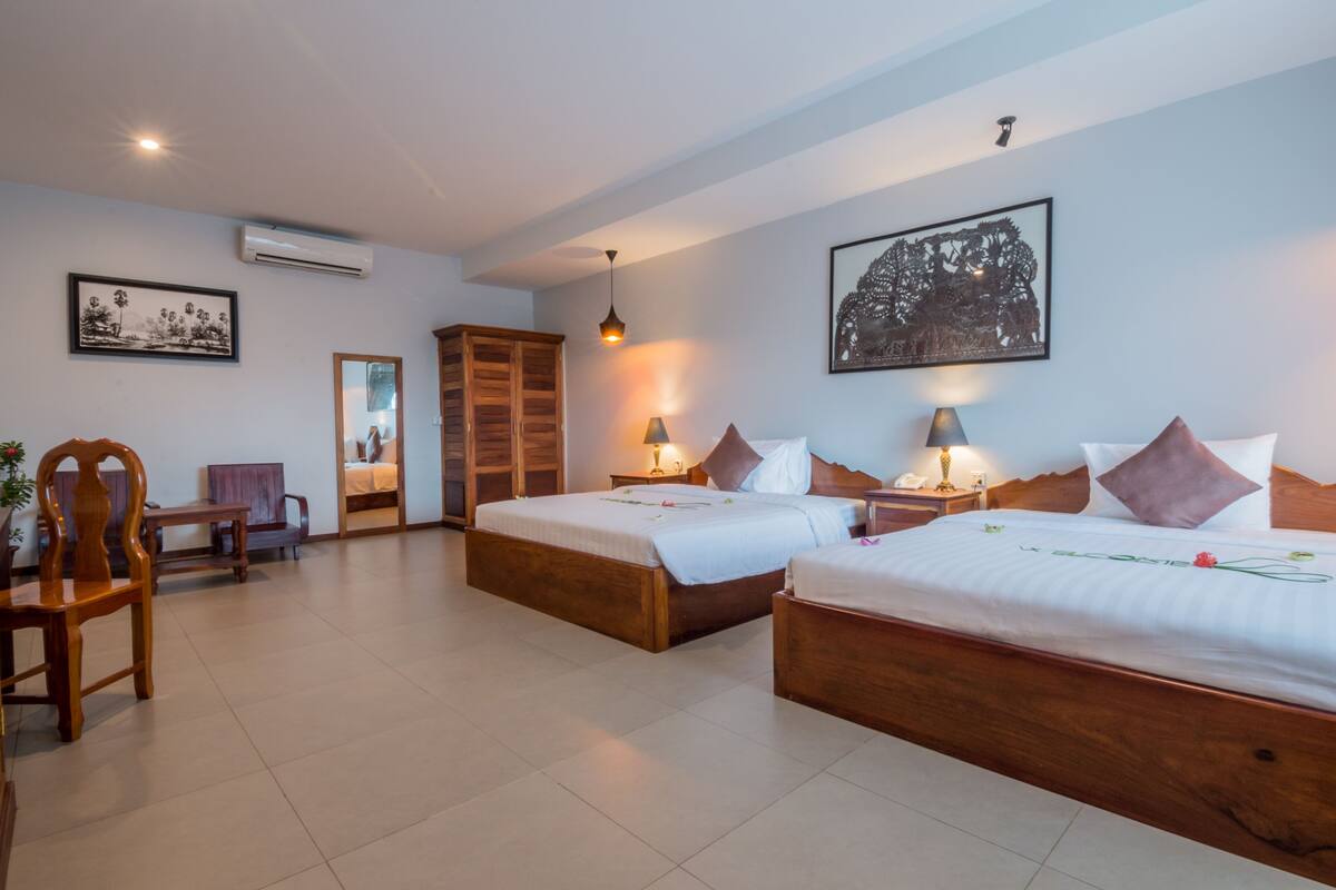 A hotel room with two wooden beds, a sitting area with a chair and table, and artwork on the walls.