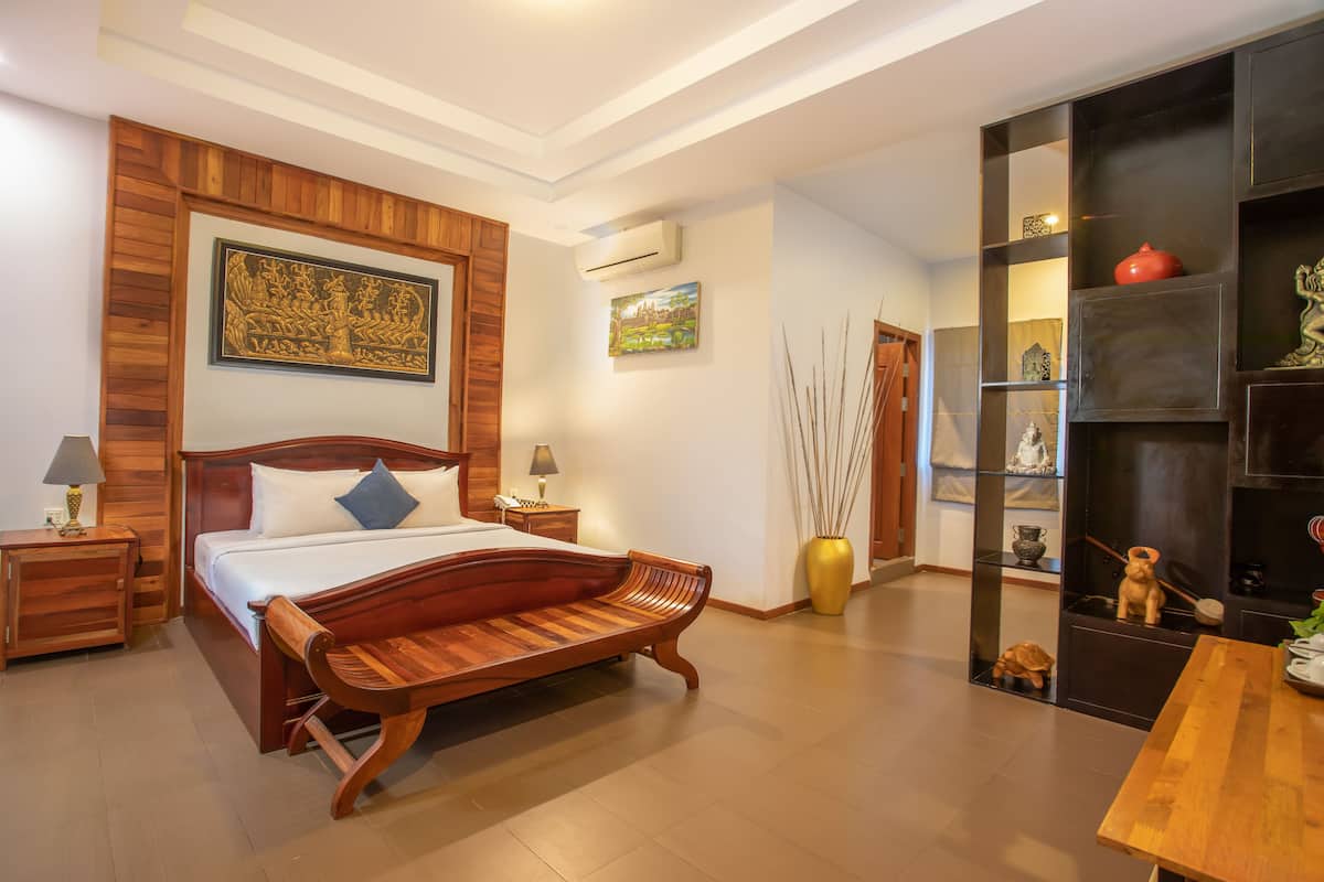 A bedroom with a wooden bed, bedside tables, a nightstand, a large vase, and a shelf with decorative items.