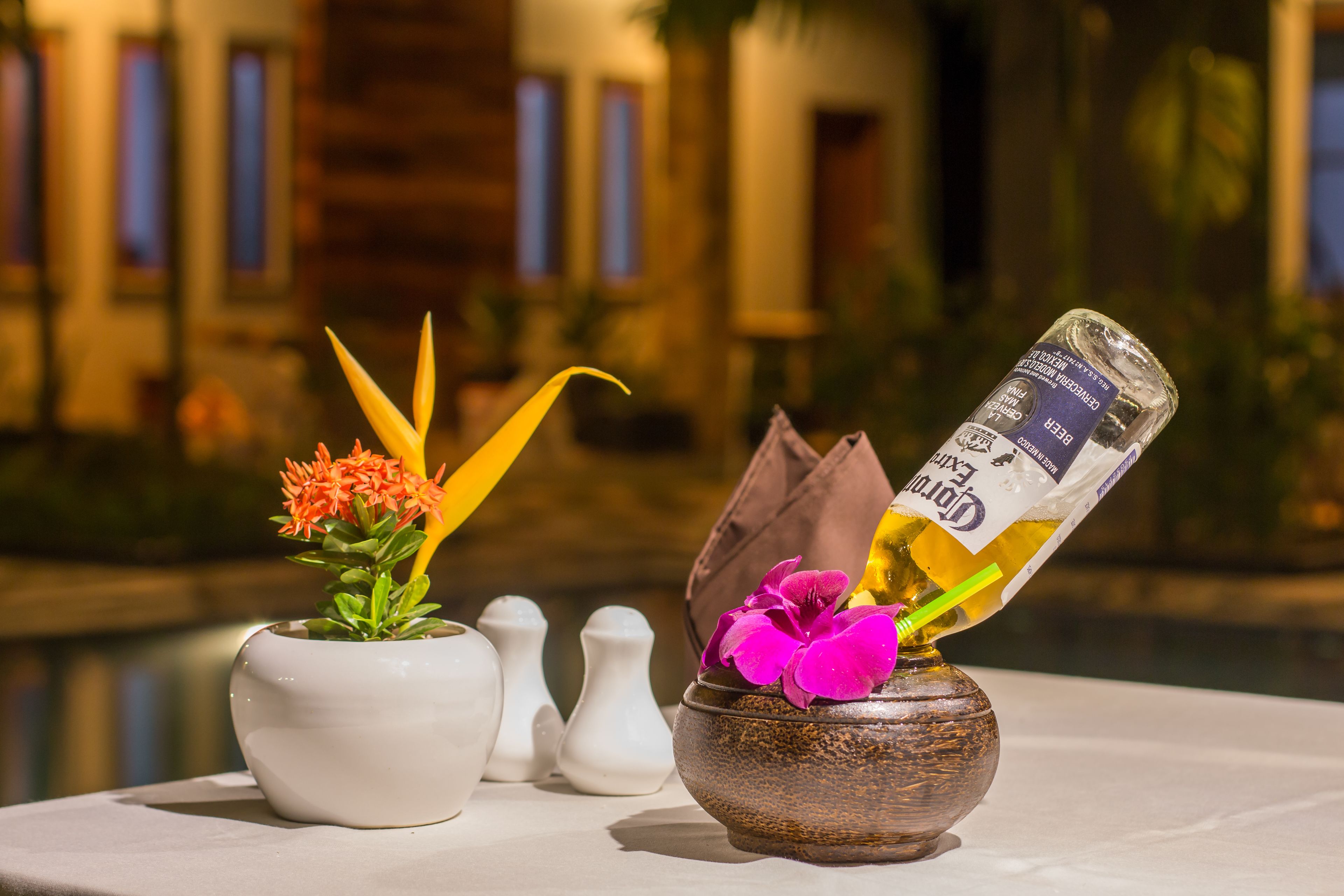 A table with two vases, one containing orange flowers and the other with a purple flower, and a bottle of Corona beer.